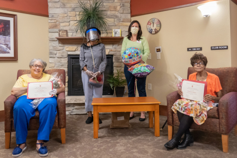 four women in a room, two standing in back and two sitting in front displaying certificates