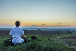 person sitting on grass looking at serene ocean landscape at sunrise