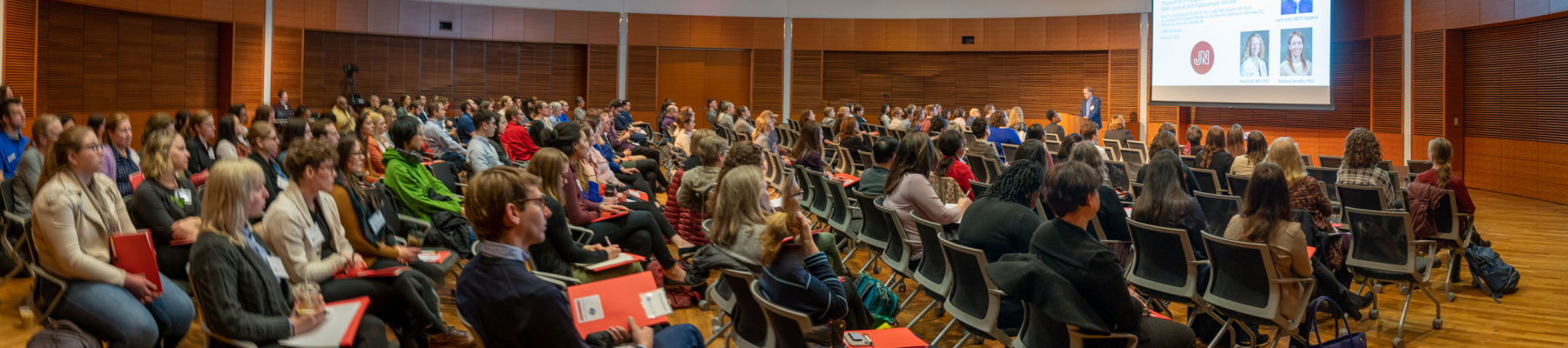 group of more than 100 people sitting in a conference room viewing a presentation