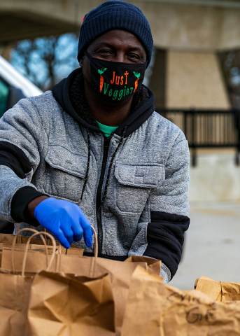man wearing facemask with words Just Veggiez and bags of food