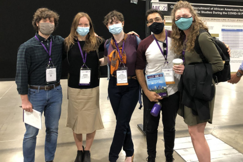a group of five people with their arms around each other wearing masks in the middle of a scientific poster session 