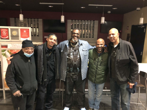 Photo from Men's Self-Care Workshop of group at movie night event. James Bester, group leader, is in the center with two men on each side of him.