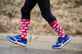 photo shows legs of someone running with blue tennis shoes and red University of Wisconsin socks