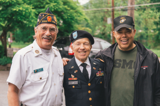 Three Veterans standing in a row and smiling with their arms around each other