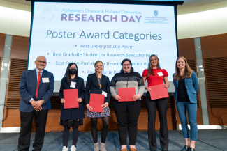 a group of four female students holding red folders containing poster award certificates flanked by faculty advisors