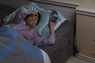 Woman in bed at night with clock in her hand