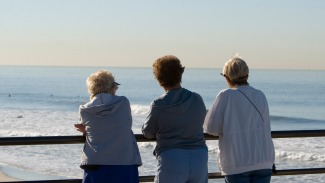 Three older women look out at the lake or sea, their backs facing the camera