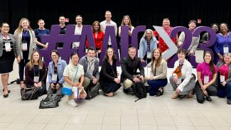 A group of researchers from the Wisconsin Alzheimer's Disease Research Center (ADRC) surrounding a sign for #AAIC23 at the Alzheimer's Association International Conference in July 2023