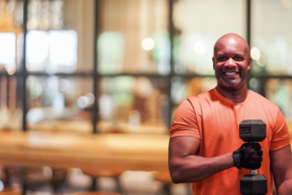 Fitness instructor Johnny Winston holding a barbell in front of a wall of windows.