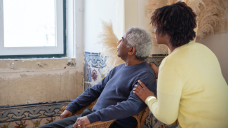 Stock photo of an older man looking out a window with a younger woman looking over him.