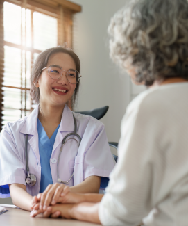 A doctor smiling as she holds an older adult's hand