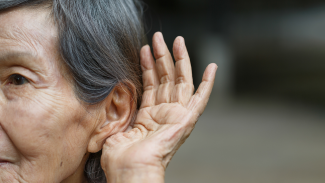 An older adult holding their hand up to their ear