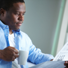 man holding cup of coffee and reading newspaper