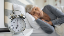 A photo of an older woman sleeping, with an alarm clock in the foreground