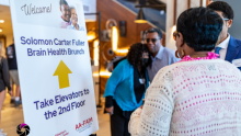 A group in front of a wayfinding sign pointing to head upstairs for the 2023 Solomon Carter Fuller Brain Health Brunch event