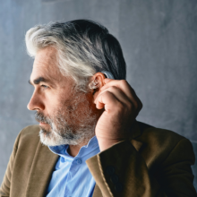 An older man facing the side is adjusting a hearing aid in his ear