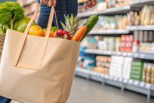 Person holding a grocery bag of healthy foods while viewing a shelf of ultra processed foods